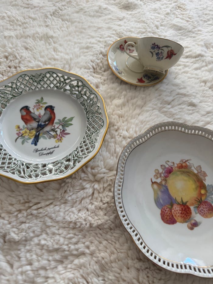 A collection of vintage ceramic plates and cup with floral and bird designs.