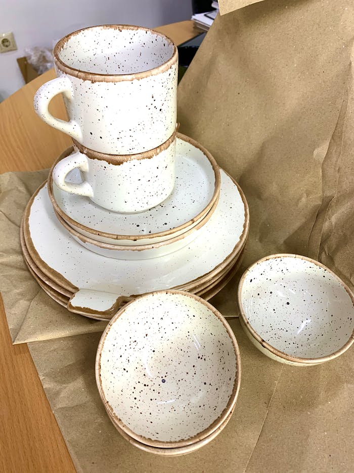 Elegant speckled ceramic dinnerware set arranged on brown paper, shot from a high angle.